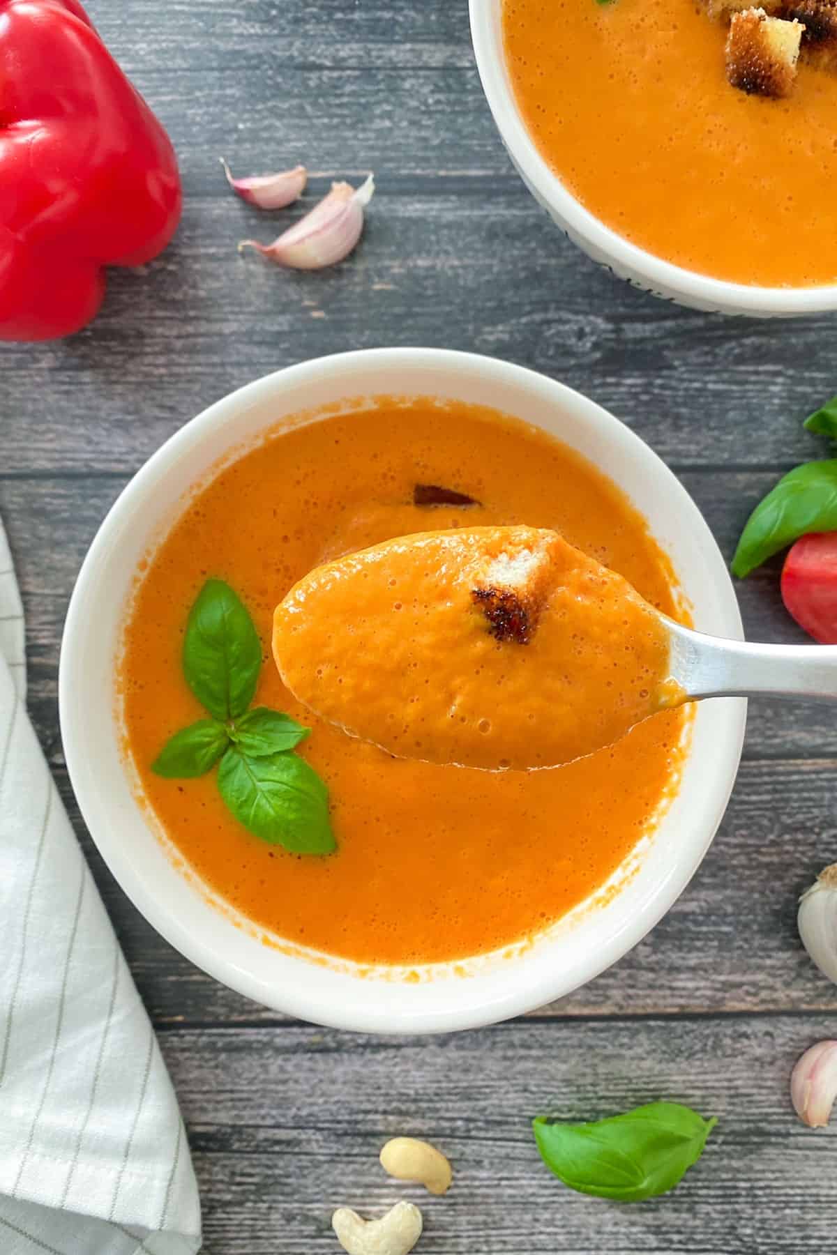Spoonful of tomato soup being held over bowl.
