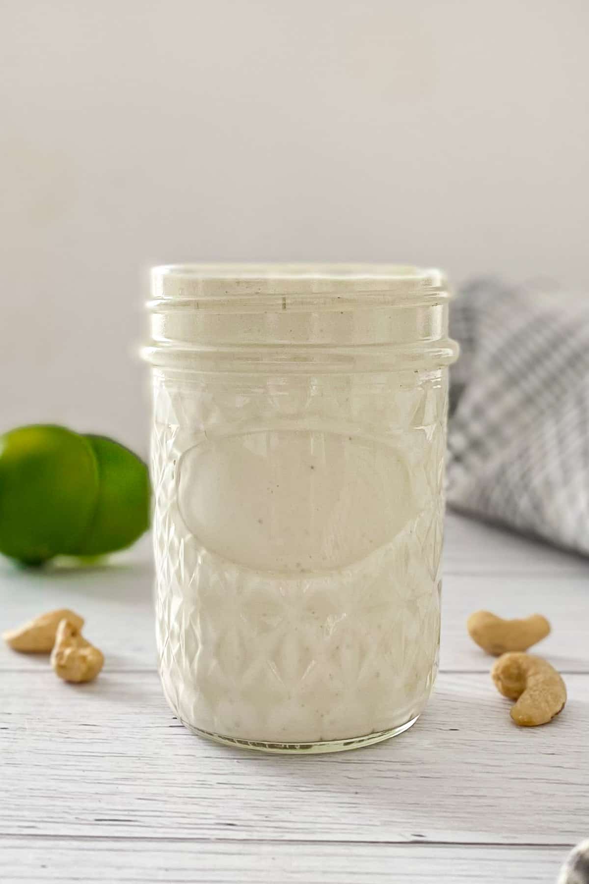 Glass jar filled with white sauce and limes in the background.