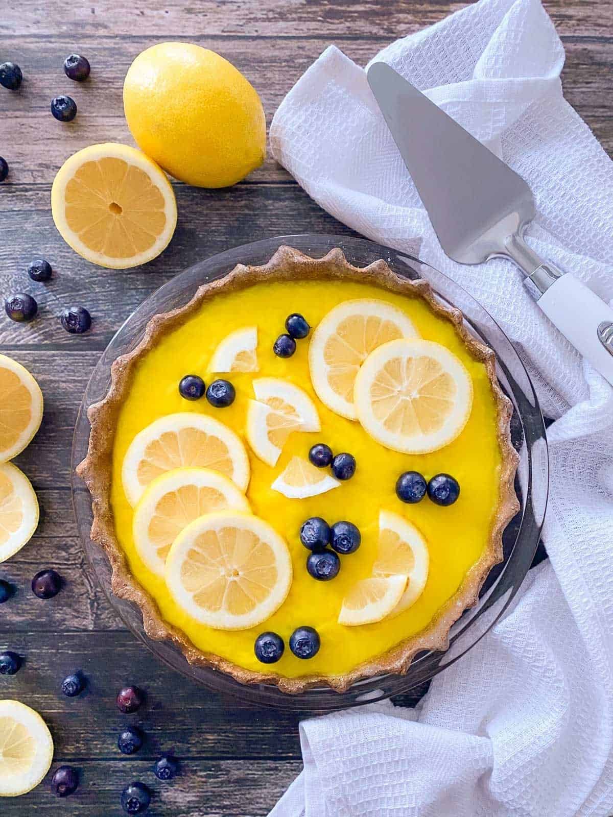 Lemon pie with lemon slices and blueberries on top in glass pie plate.