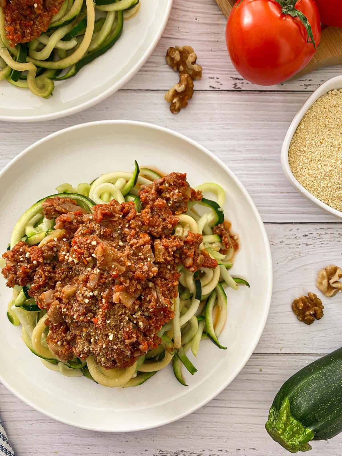 Plate of zucchini noodles with vegan bolognese sauce and parmesan cheese on top.