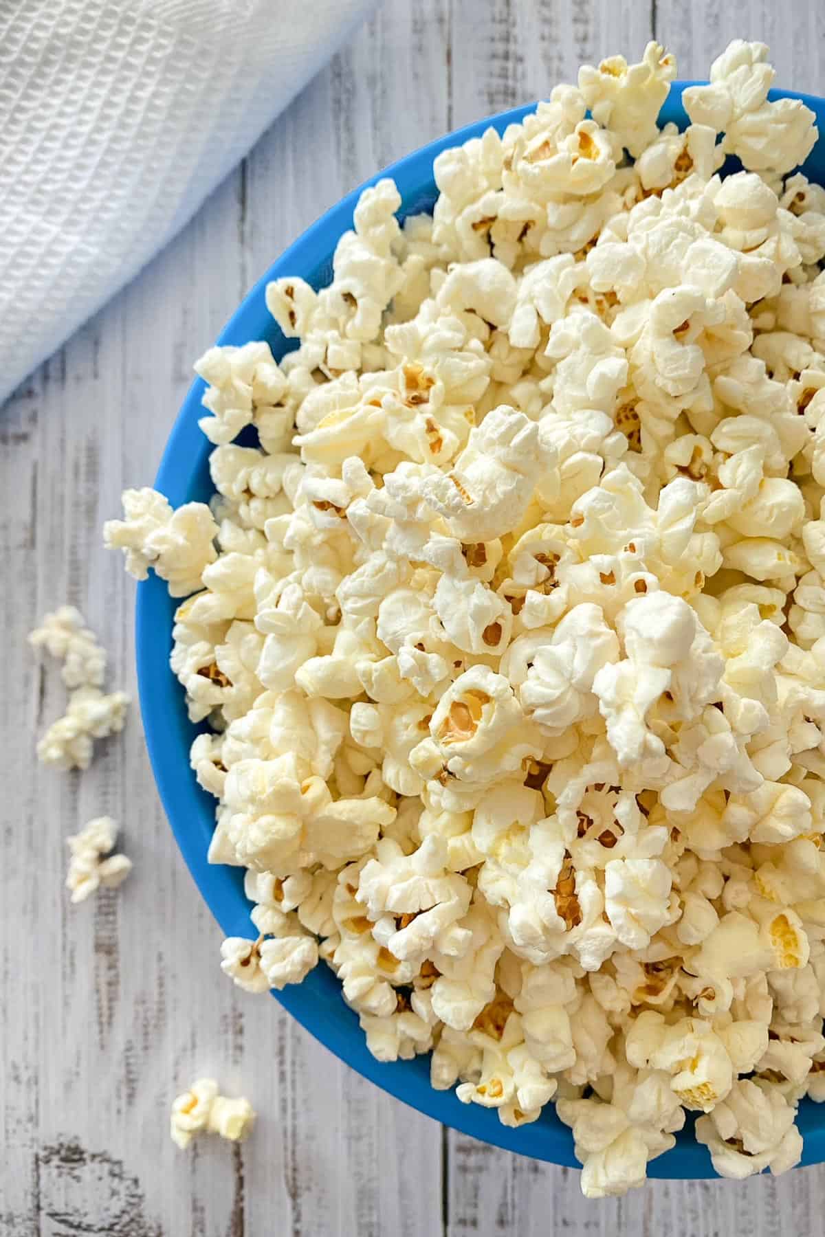 Blue bowl overfilled with popcorn that's spilling over the sides.
