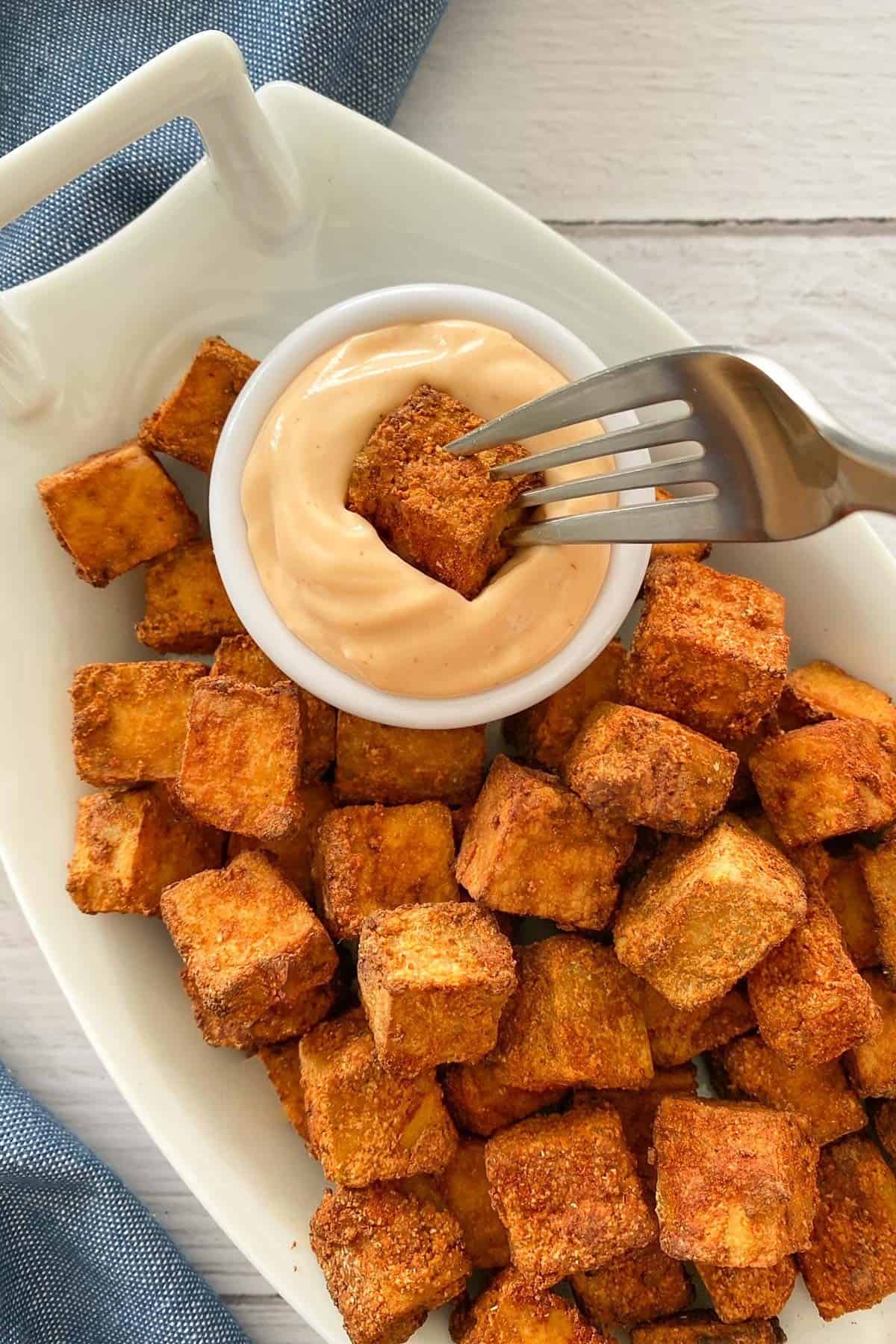 Fork dunking cube of tofu into spicy mayo dip.