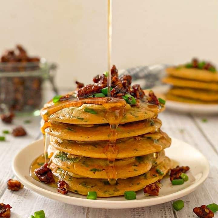 Stack of pancakes with bacon and chives on top and syrup dripping down.