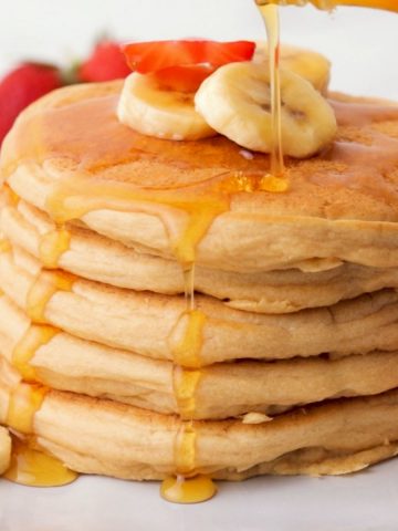 stack of vegan pancakes with banana slices on top and syrup dripping down.