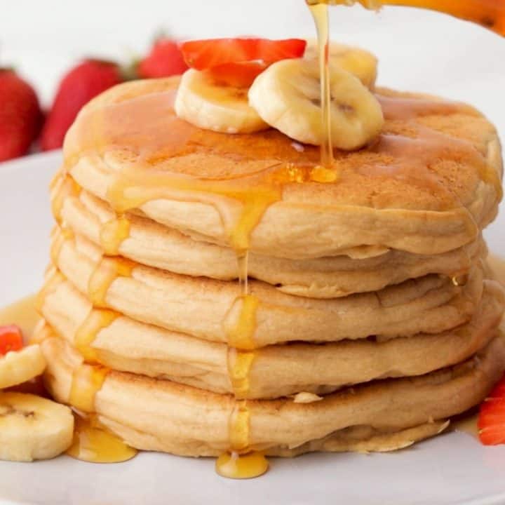 stack of vegan pancakes with banana slices on top and syrup dripping down.