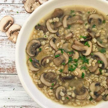 White bowl of mushroom barley soup with parsley garnish.