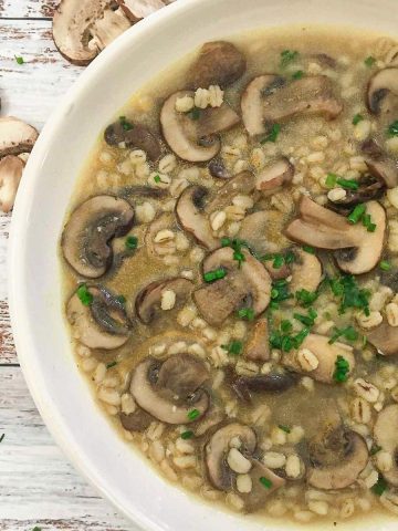 White bowl of mushroom barley soup with parsley garnish.