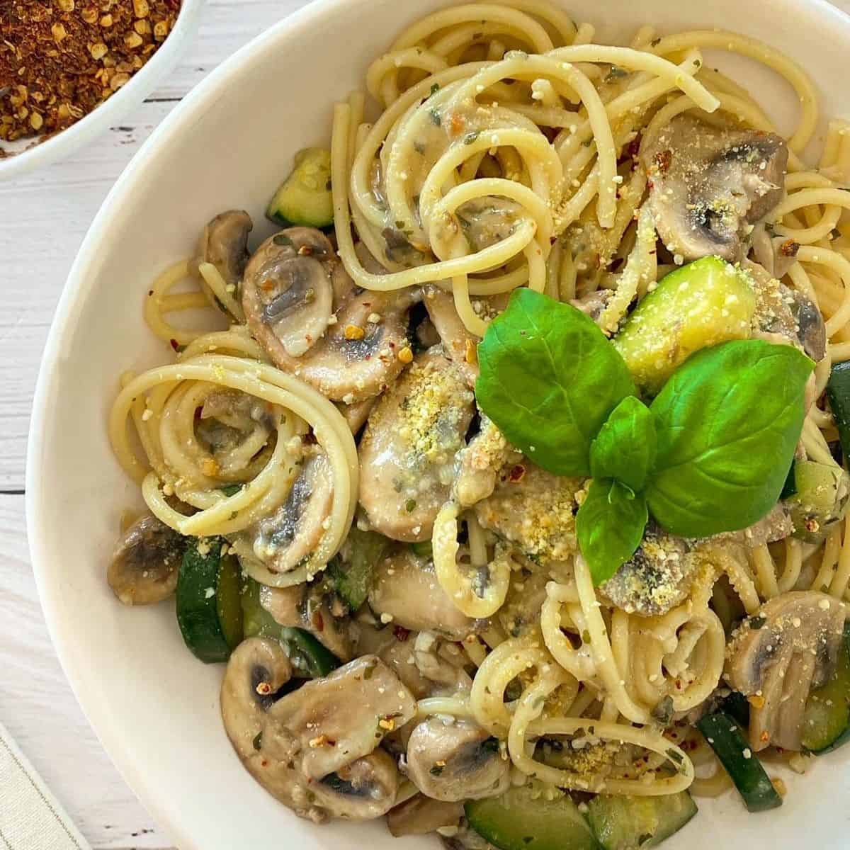 Plate of spaghetti, zucchini and mushrooms with basil on top.