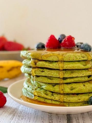 Stack of green pancakes on plate with berries on top.