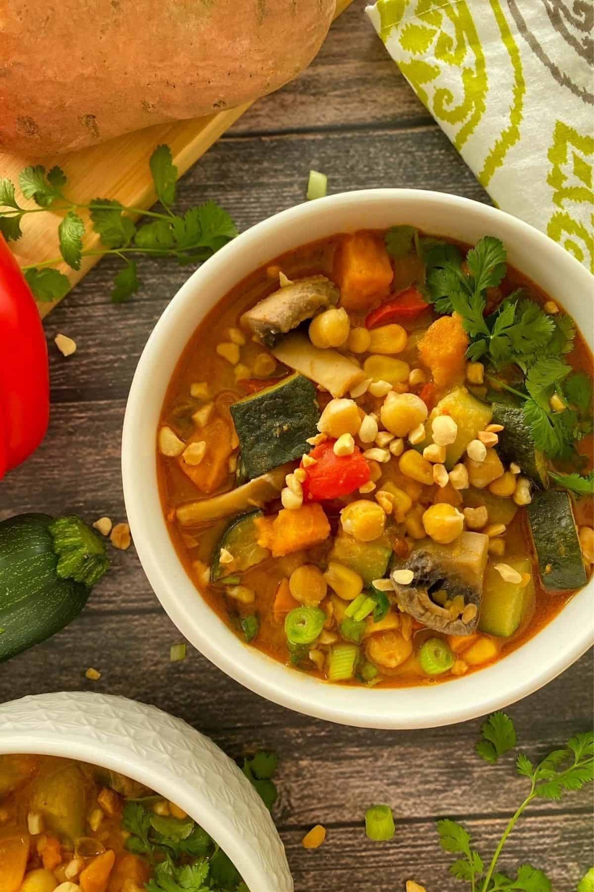 White bowl filled with vegetable and chickpea soup with peanuts on top.