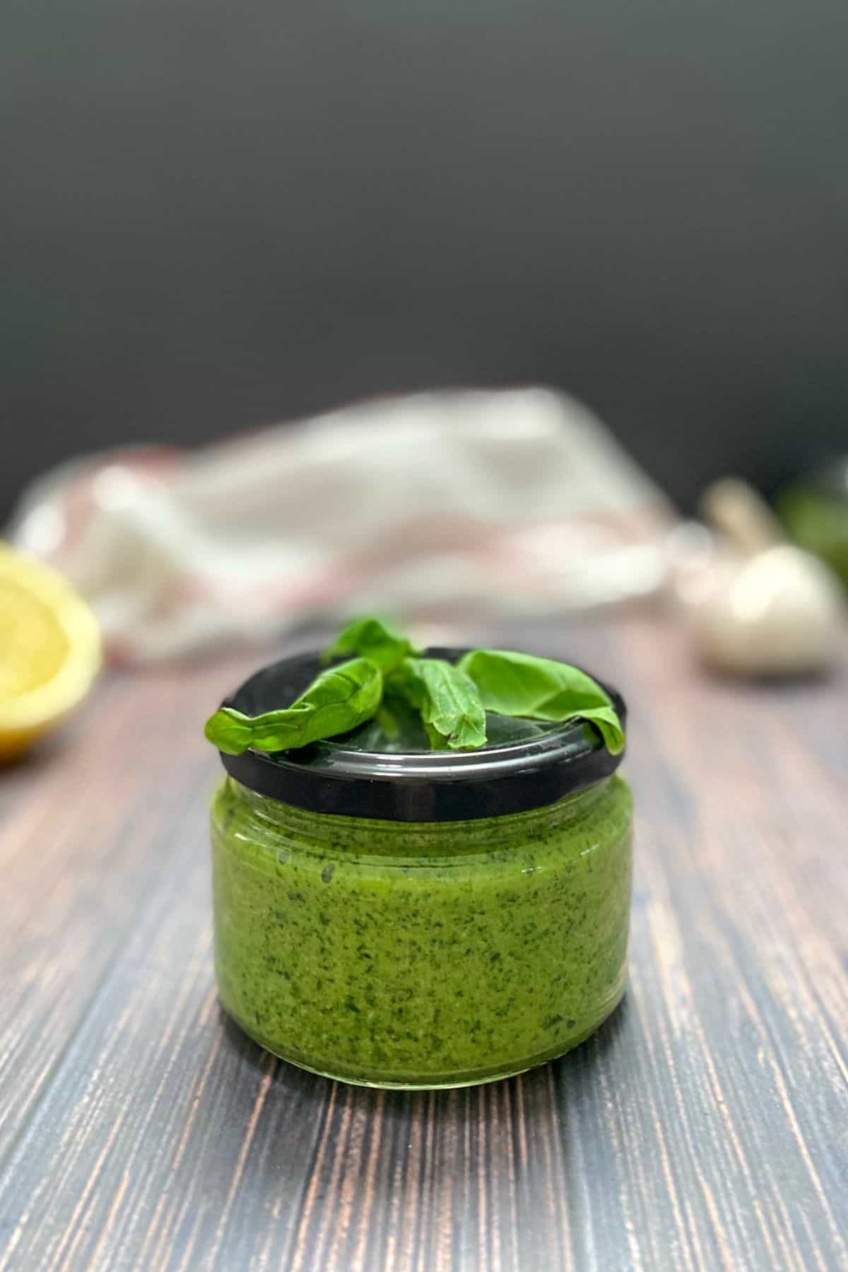 Basil pesto in sealed glass jar with pesto leaves on top.