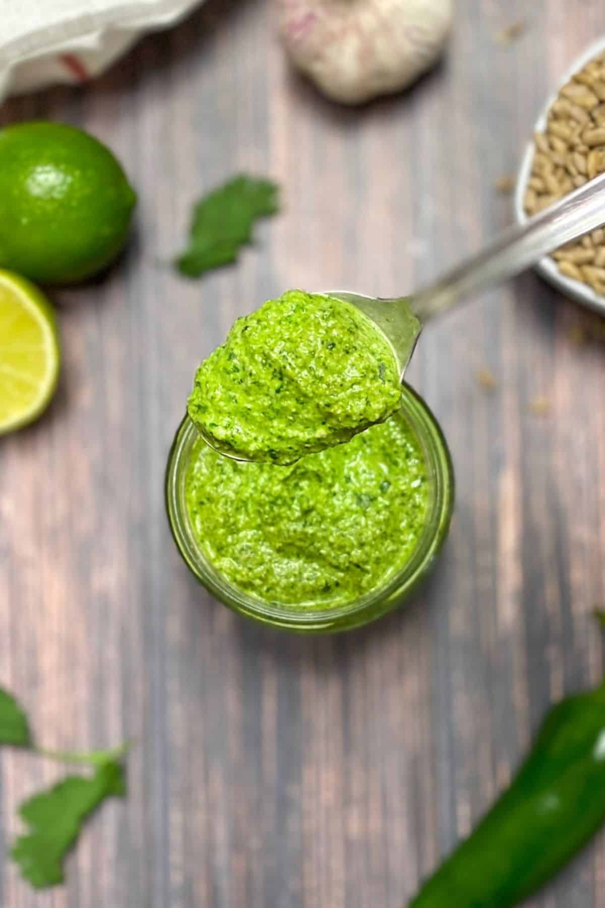 Cilantro pesto in glass jar with lime, sunflower seeds and jalapeno in the background