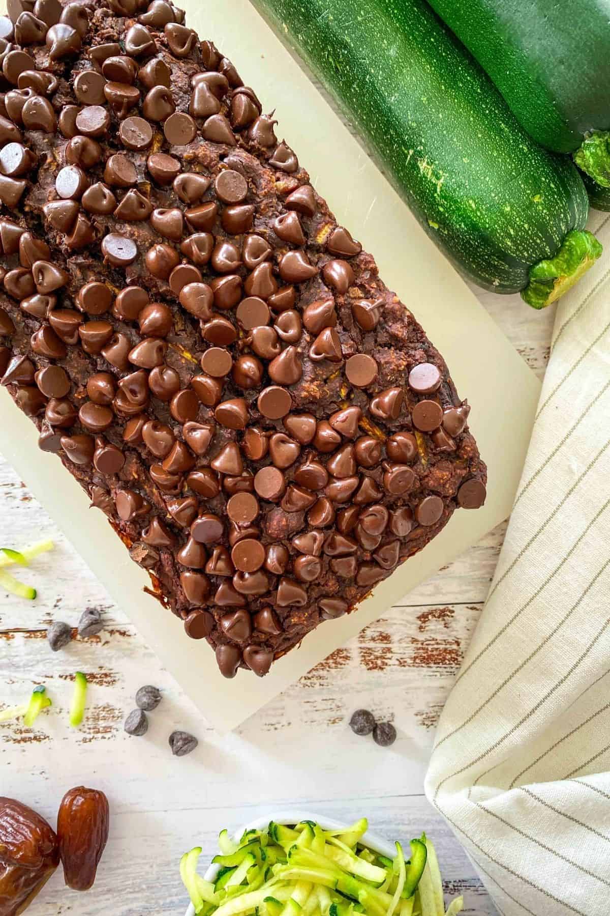 Whole loaf of double chocolate zucchini bread on cutting board with zucchini in background.
