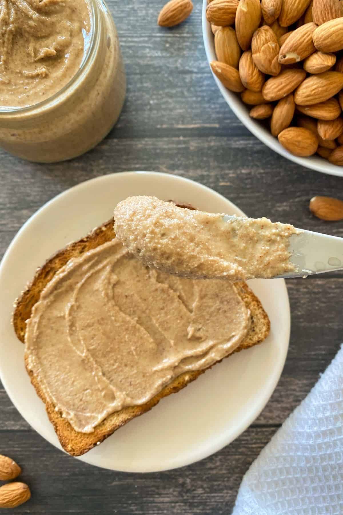 Slice of toast on plate with almond butter on top and knife with almond butter on it.