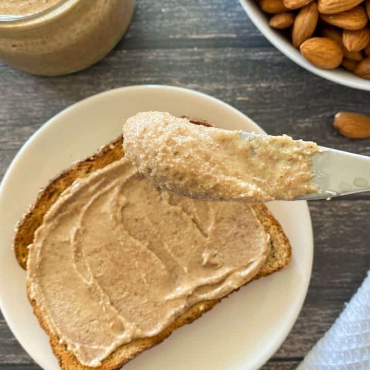 Slice of toast on plate with almond butter on top and knife with almond butter on it.