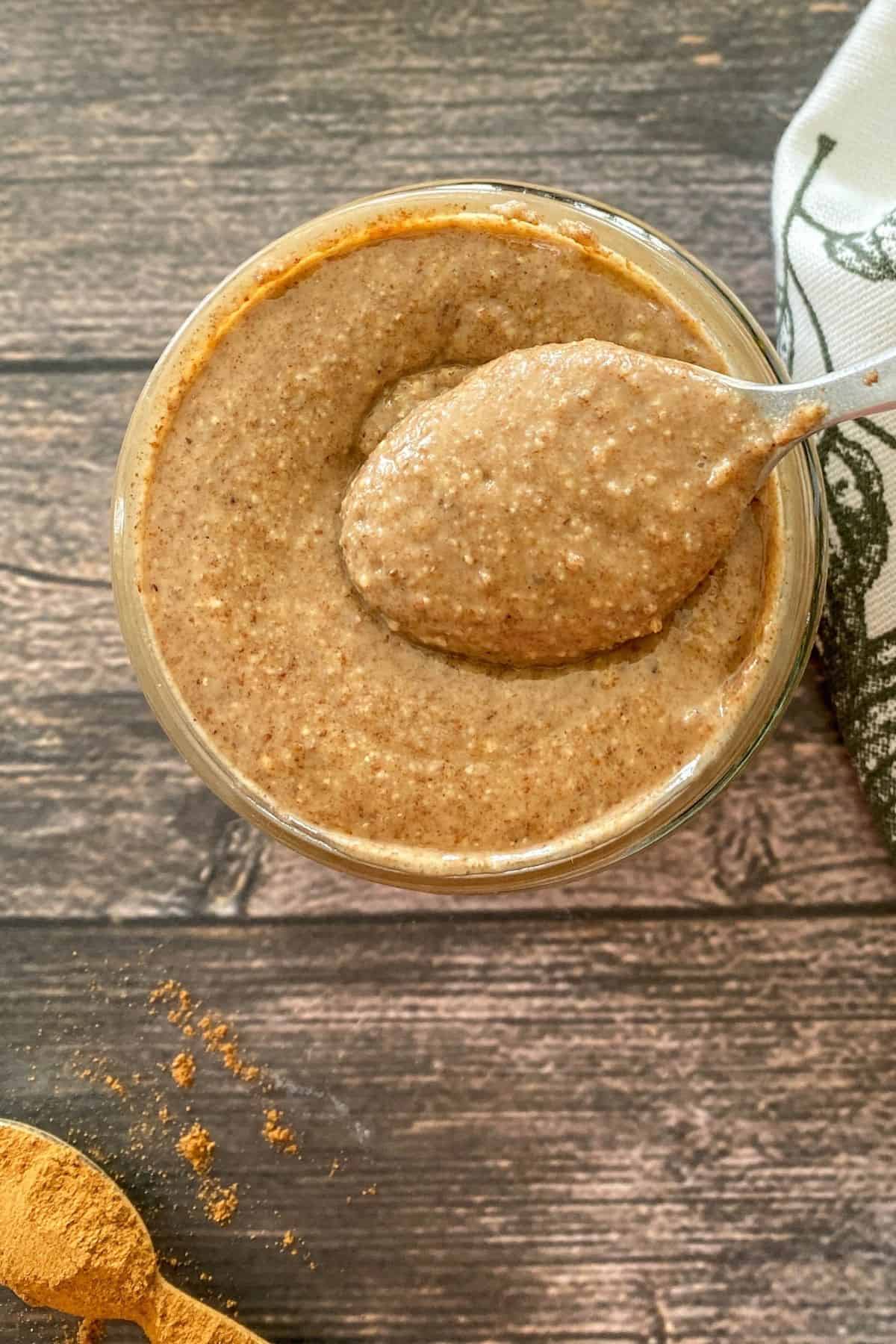 Glass jar filled with pecan butter with spoonful of it resting on top of open jar.