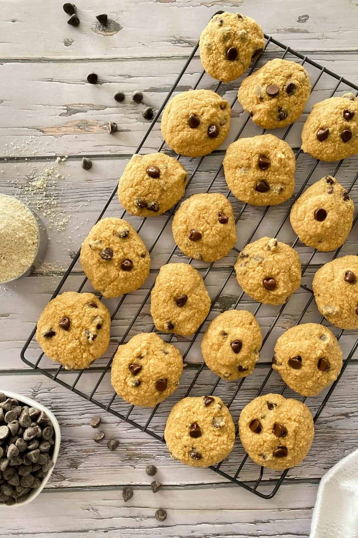 Chocolate chip cookies on wire rack with cup of flour and bowl of chocolate chips on the side.