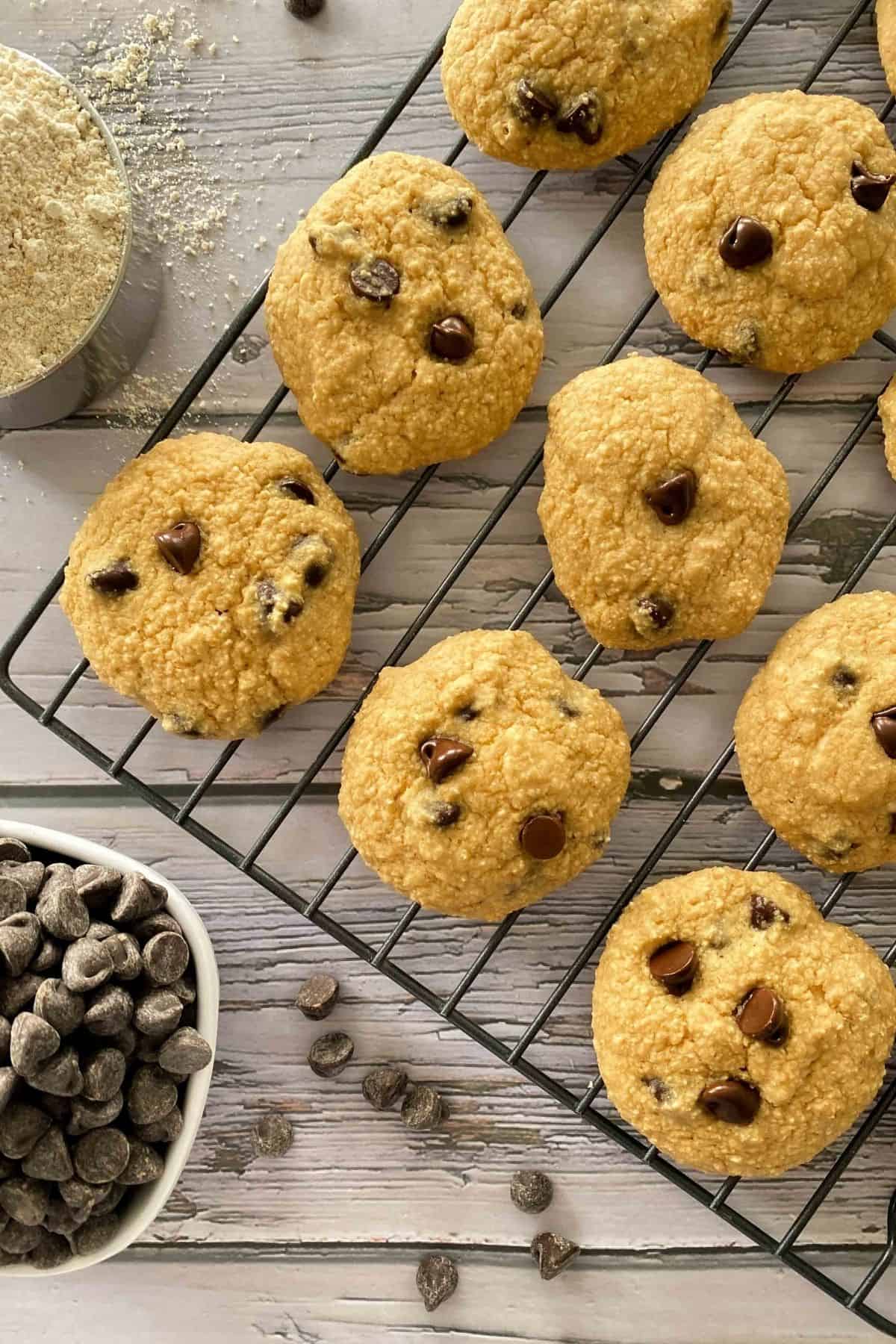 Cookies on cooling rack with cup of flour and chocolate chips on the side.