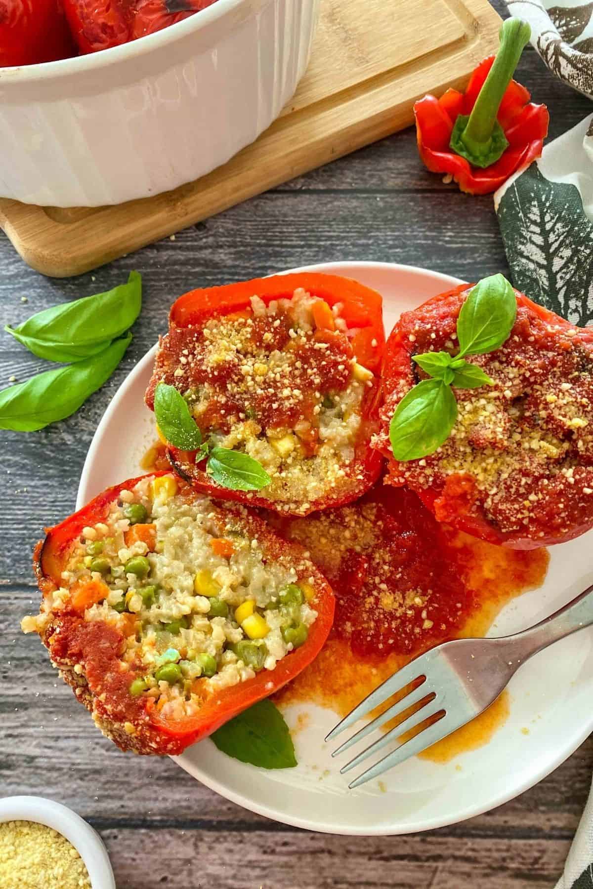 Risotto stuffed peppers in white plate with fork on the side and parmesan and basil on top.