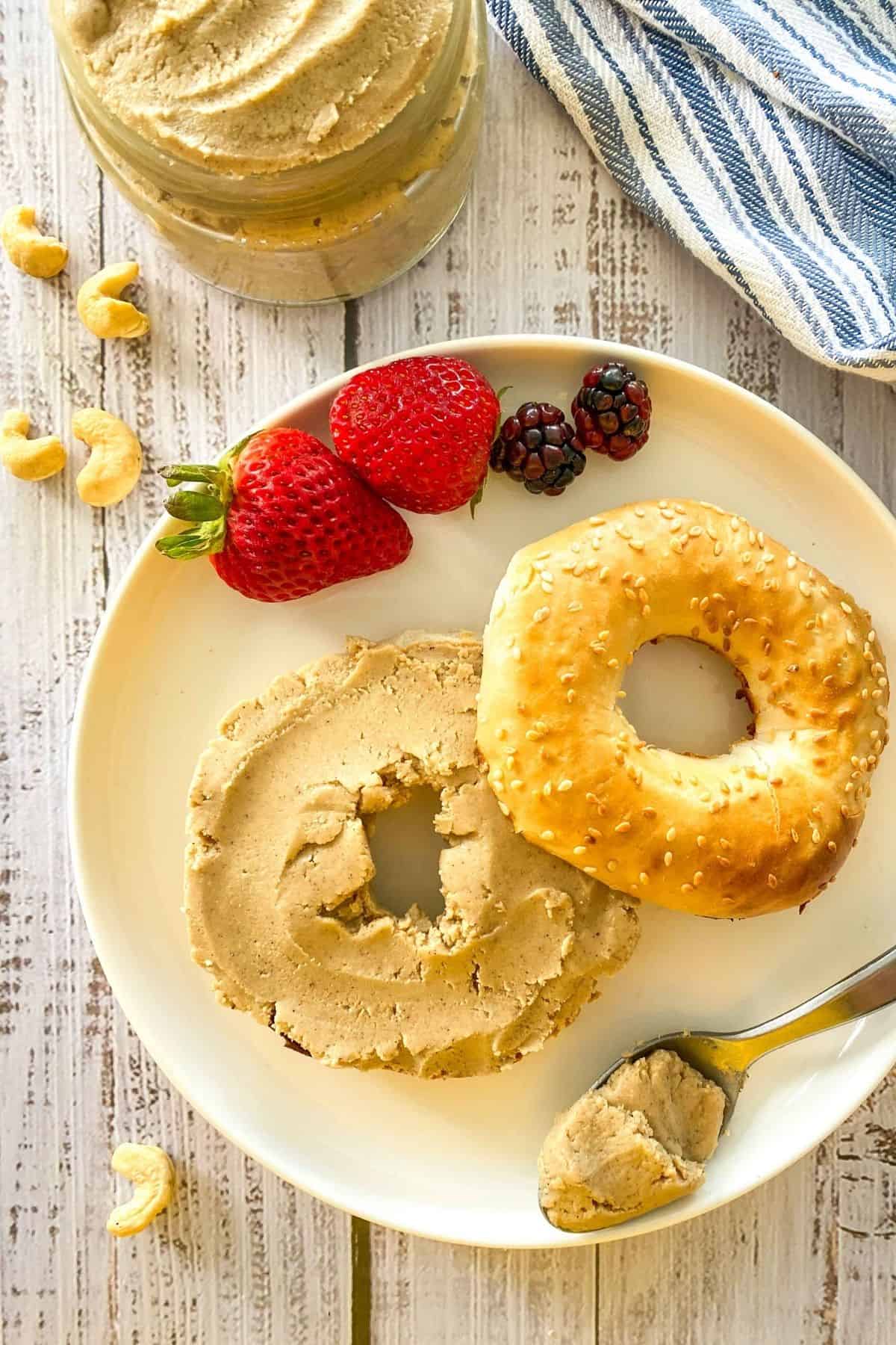 Bagel on plate with cashew butter spread on top and berries on the side.