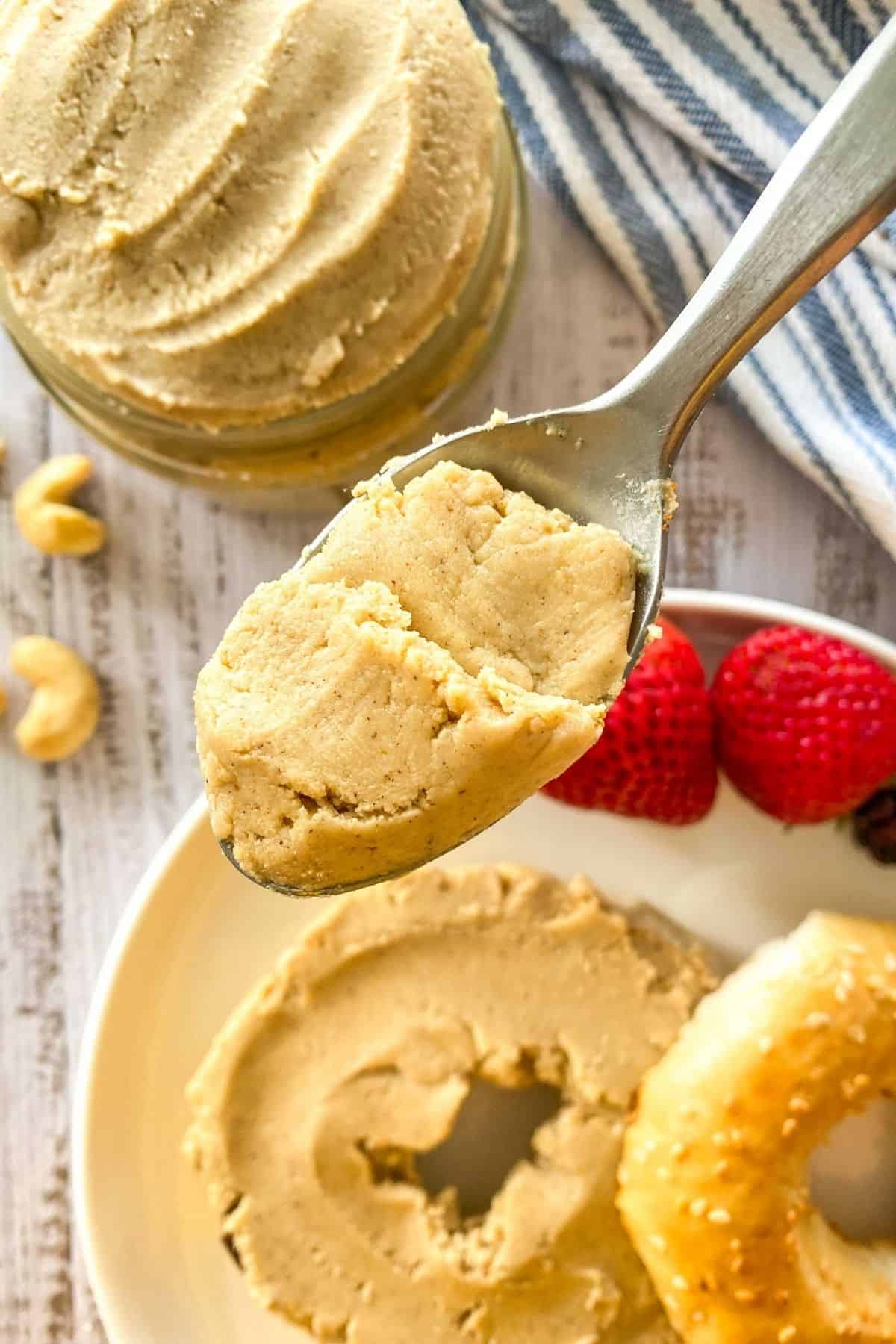 Spoonful of cashew butter held up with bagel spread with cashew butter below it.
