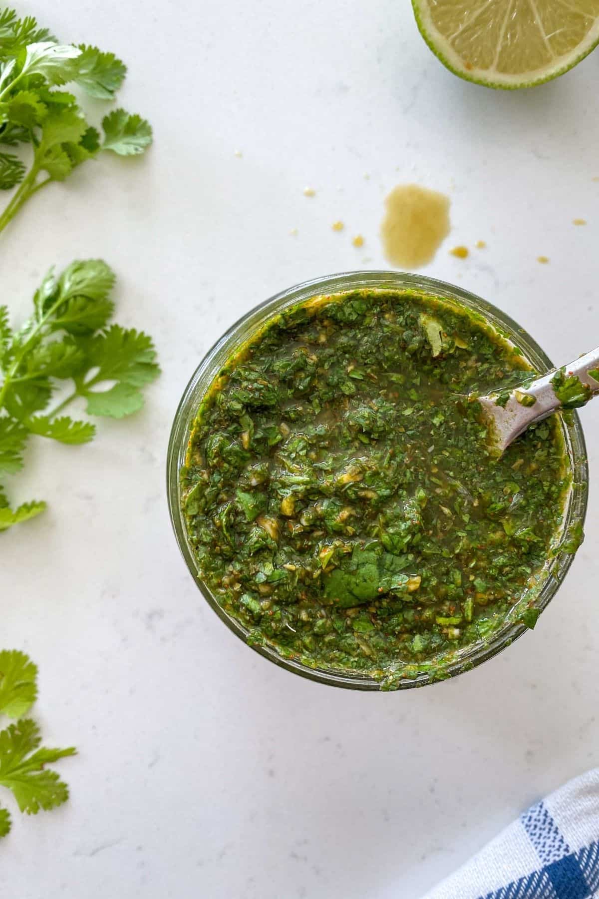 Glass jar filled with chimichurri with lime and parsley on the side.