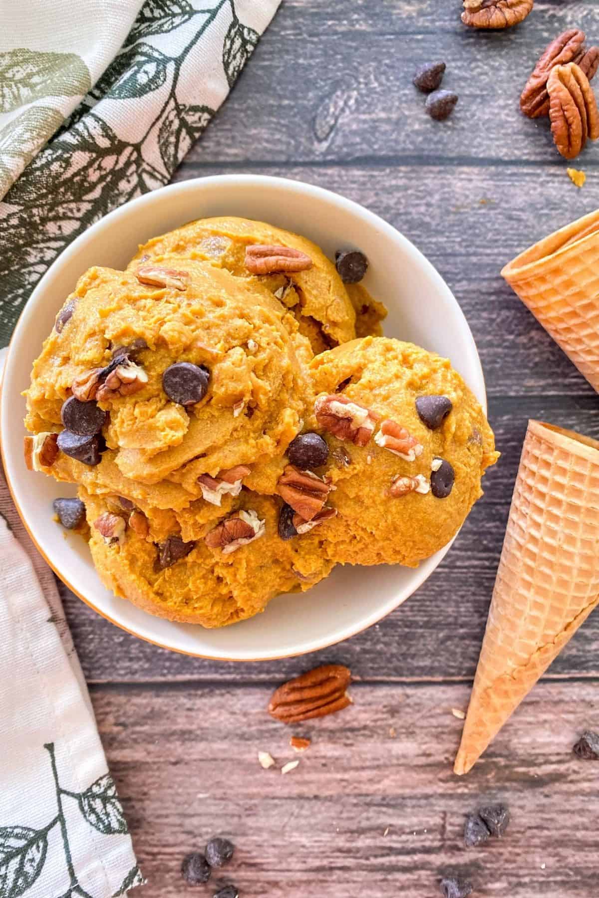 Bowl of pumpkin ice cream with chocolate chips and pecans beside it.