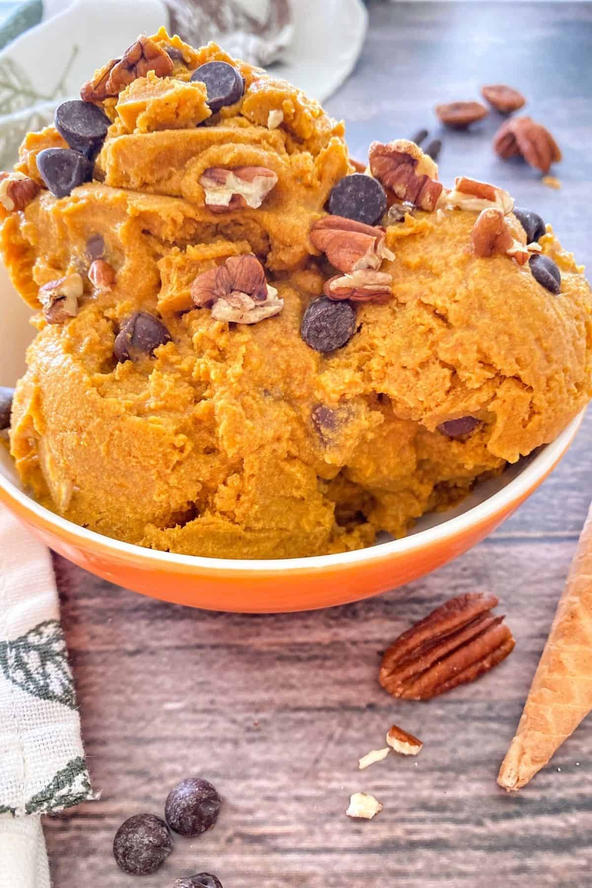 Scoops of pumpkin ice cream in bowl with pecans and chocolate chips on top.
