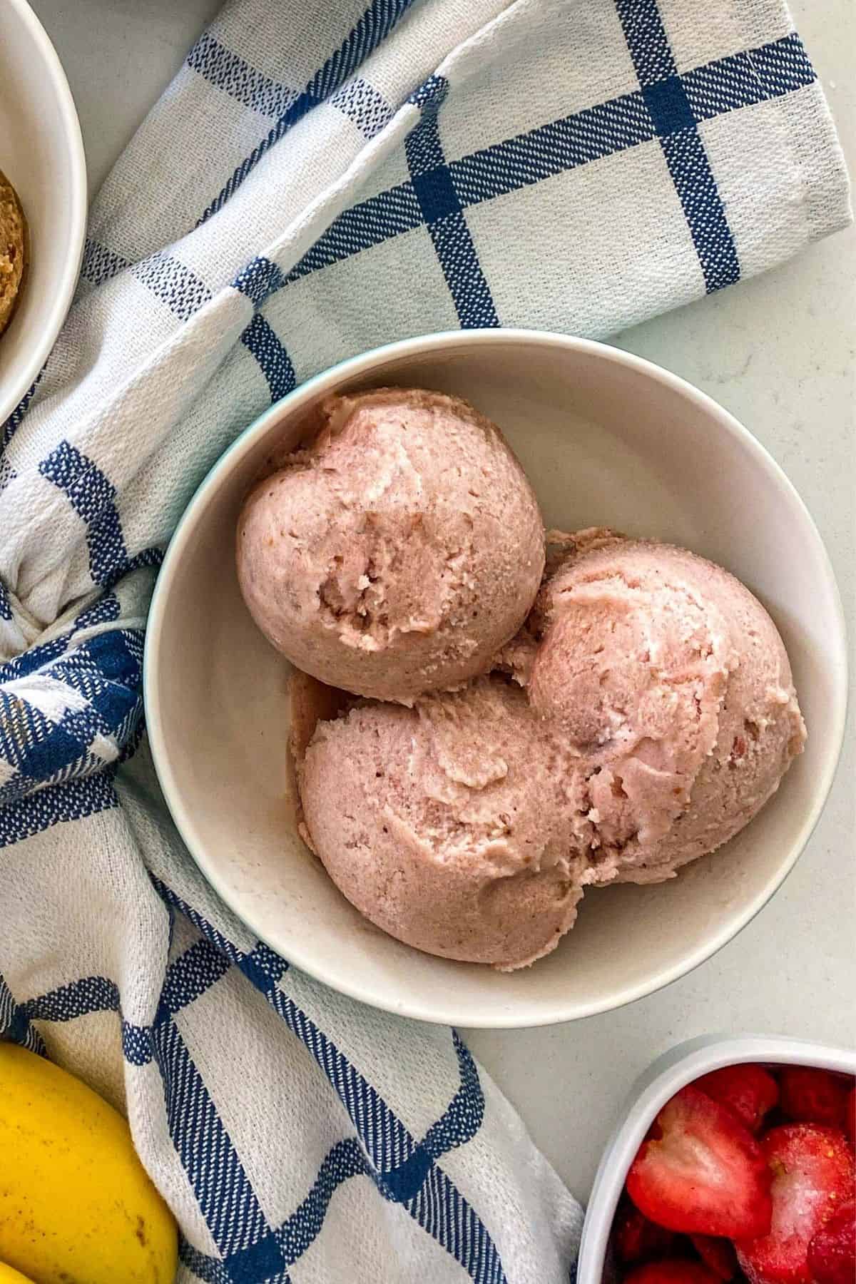 White bowl with three scoops of strawberry ice cream inside.