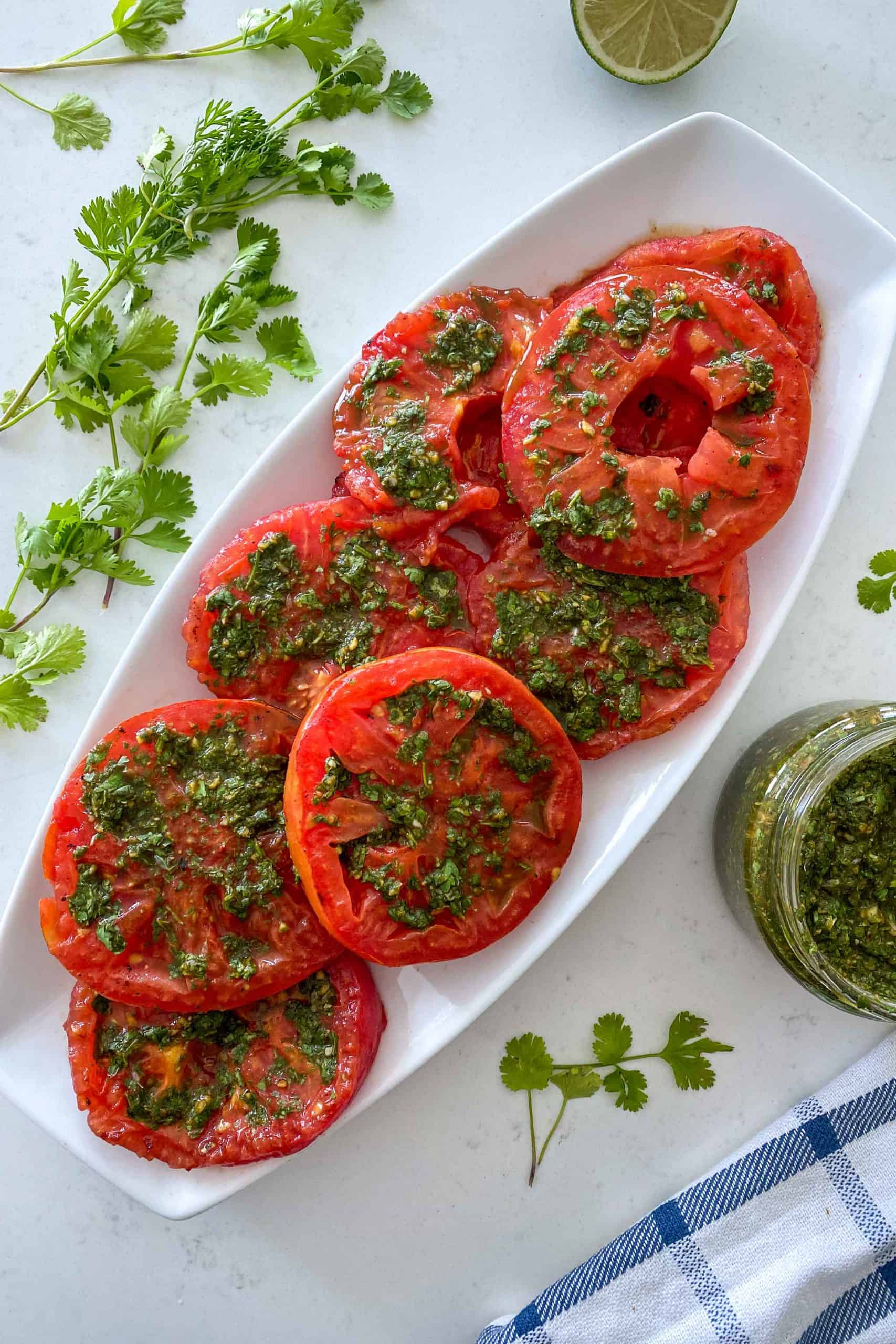 Tomato slices on white serving dish with chimichurri sauce on top.