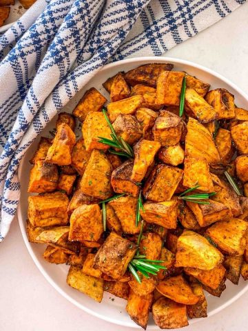 White plate with cubed sweet potatoes and rosemary garnish.