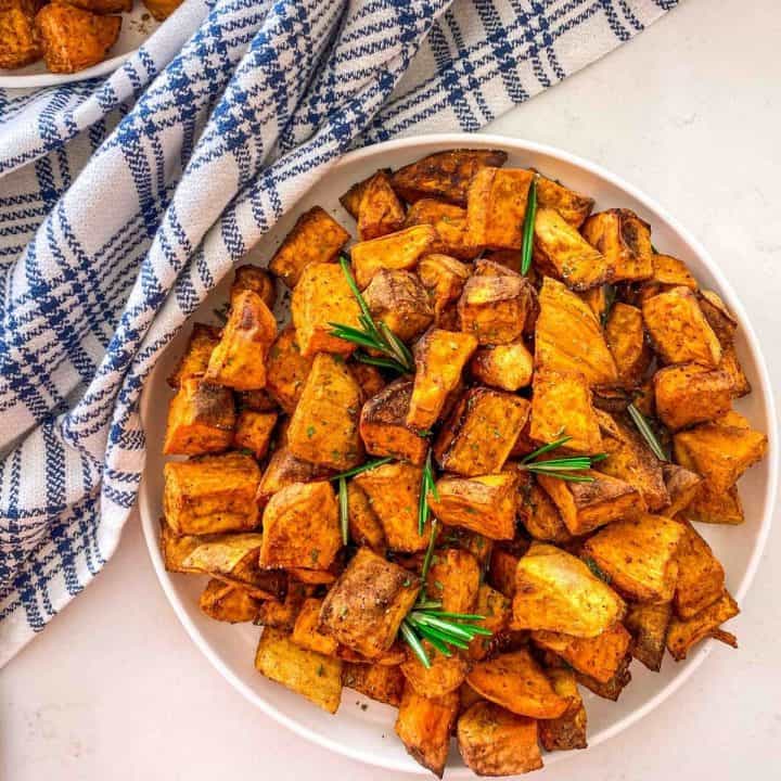 White plate with cubed sweet potatoes and rosemary garnish.