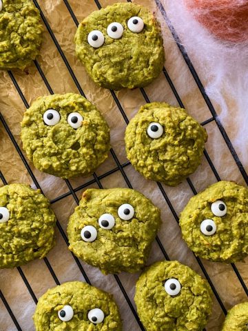 Green cookies with candy eyes on cooling rack with cobwebs around it.
