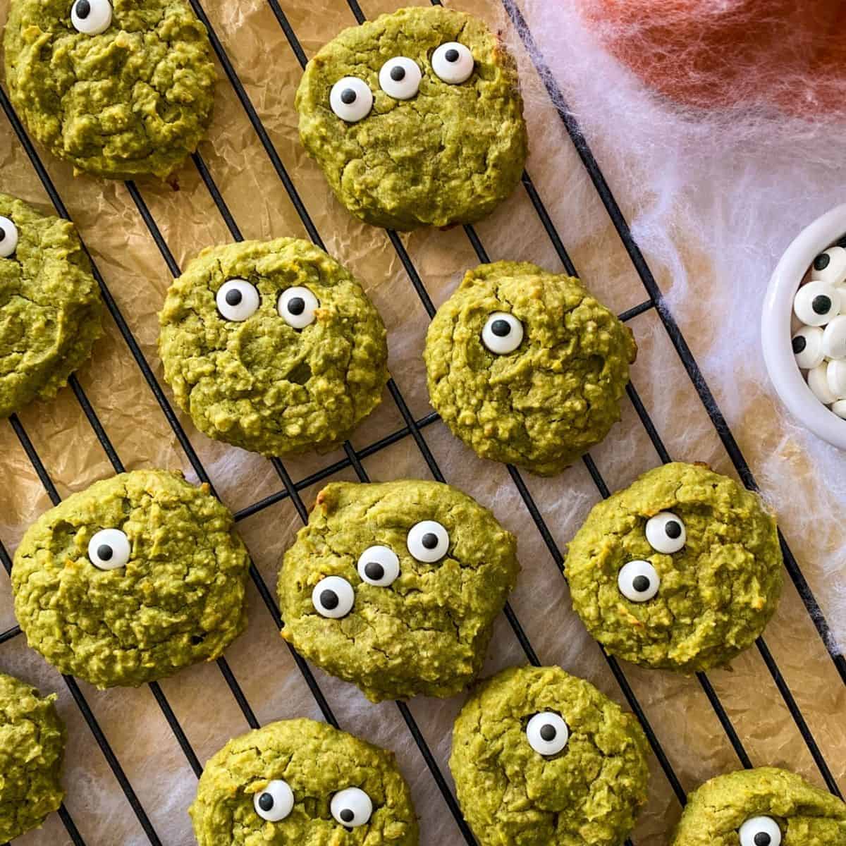 Green cookies with candy eyes on cooling rack with cobwebs around it.