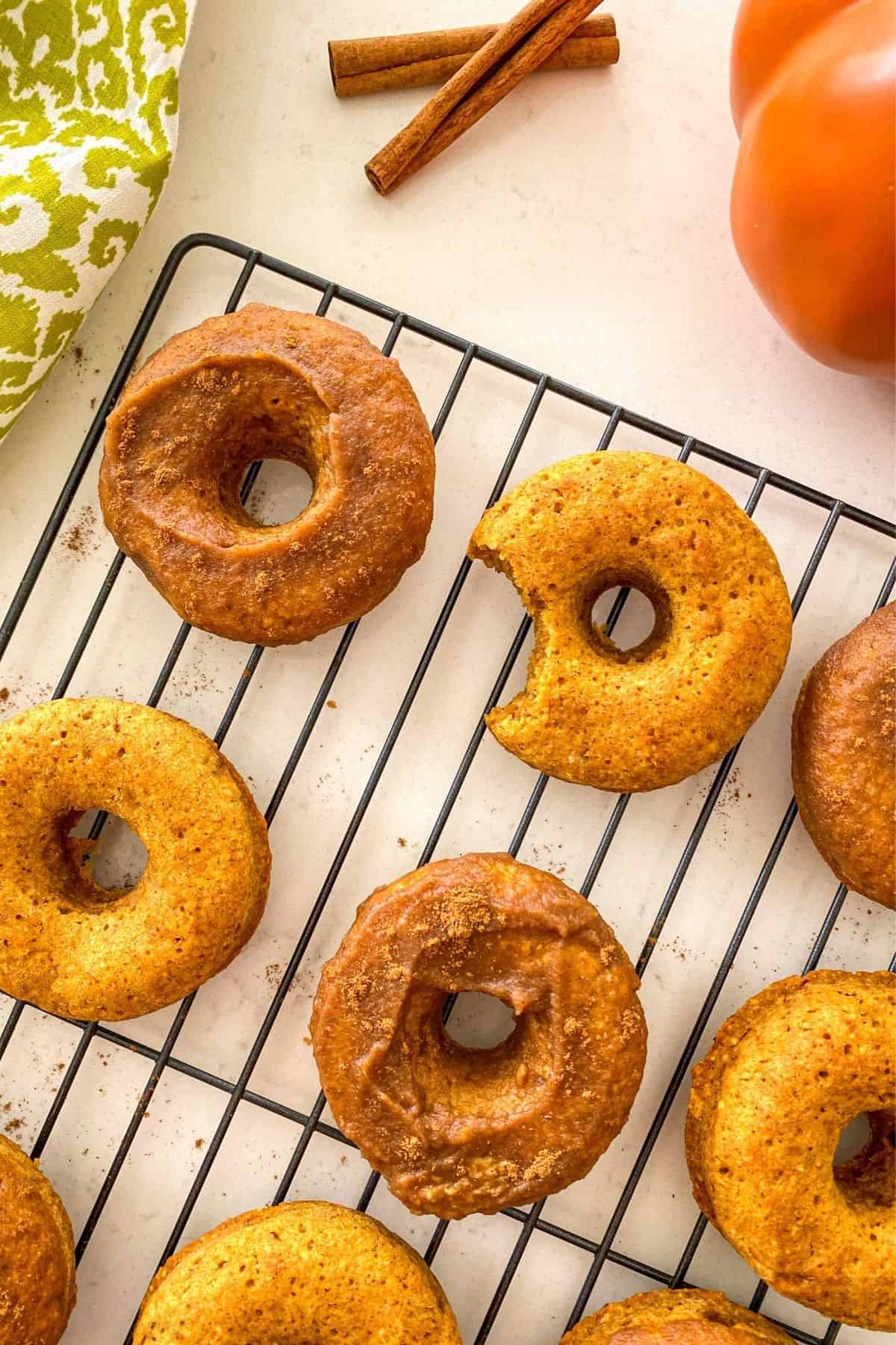Pumpkin donuts on cooling rack with bite taken out of one of them.