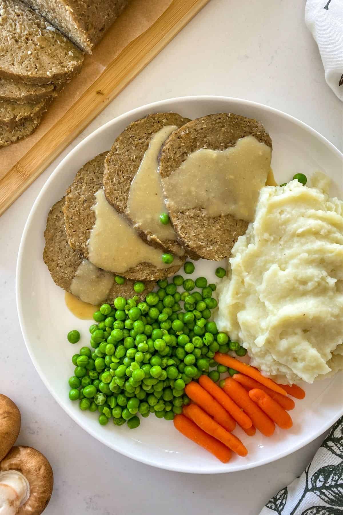 Sliced roast with gravy on top and peas, carrots and mashed potatoes beside it.