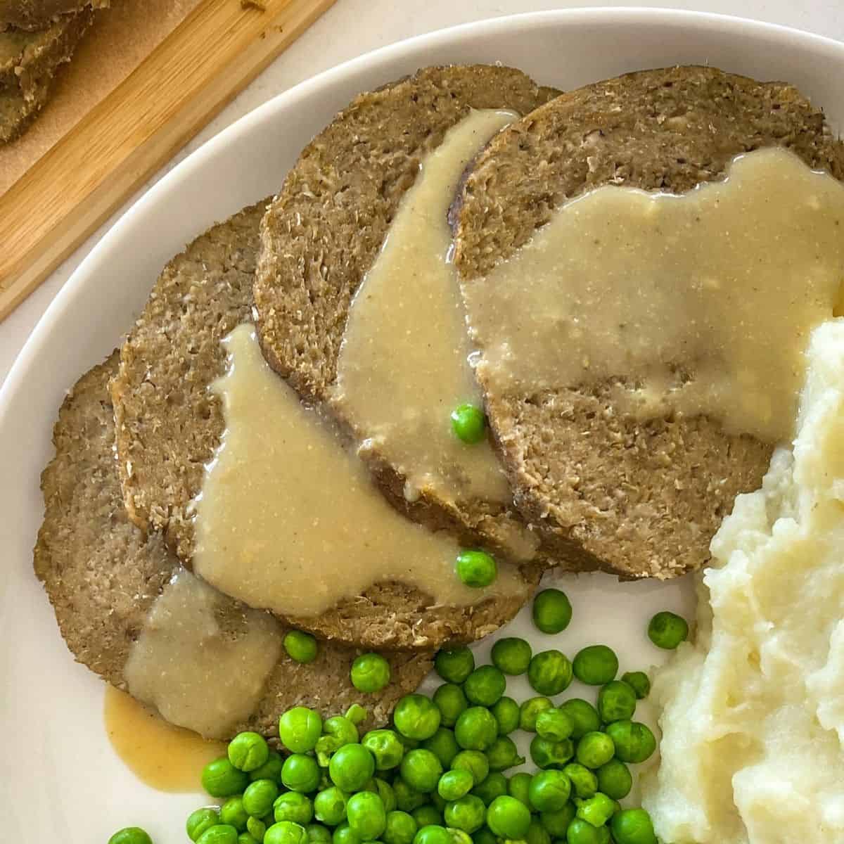 Sliced roast with gravy on top and peas and mashed potatoes beside it.