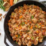 Cast iron pan filled with bread, pecans, carrots, onion and rosemary garnish.