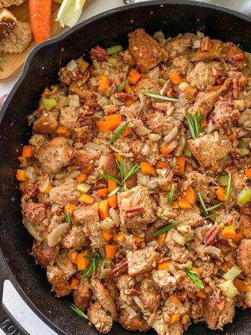 Cast iron pan filled with bread, pecans, carrots, onion and rosemary garnish.