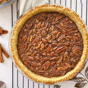 Pecan pie on cooling rack with cinnamon sticks and pecans beside it.