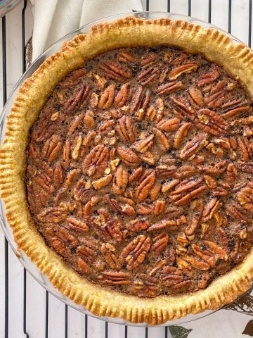 Pecan pie on cooling rack with cinnamon sticks and pecans beside it.