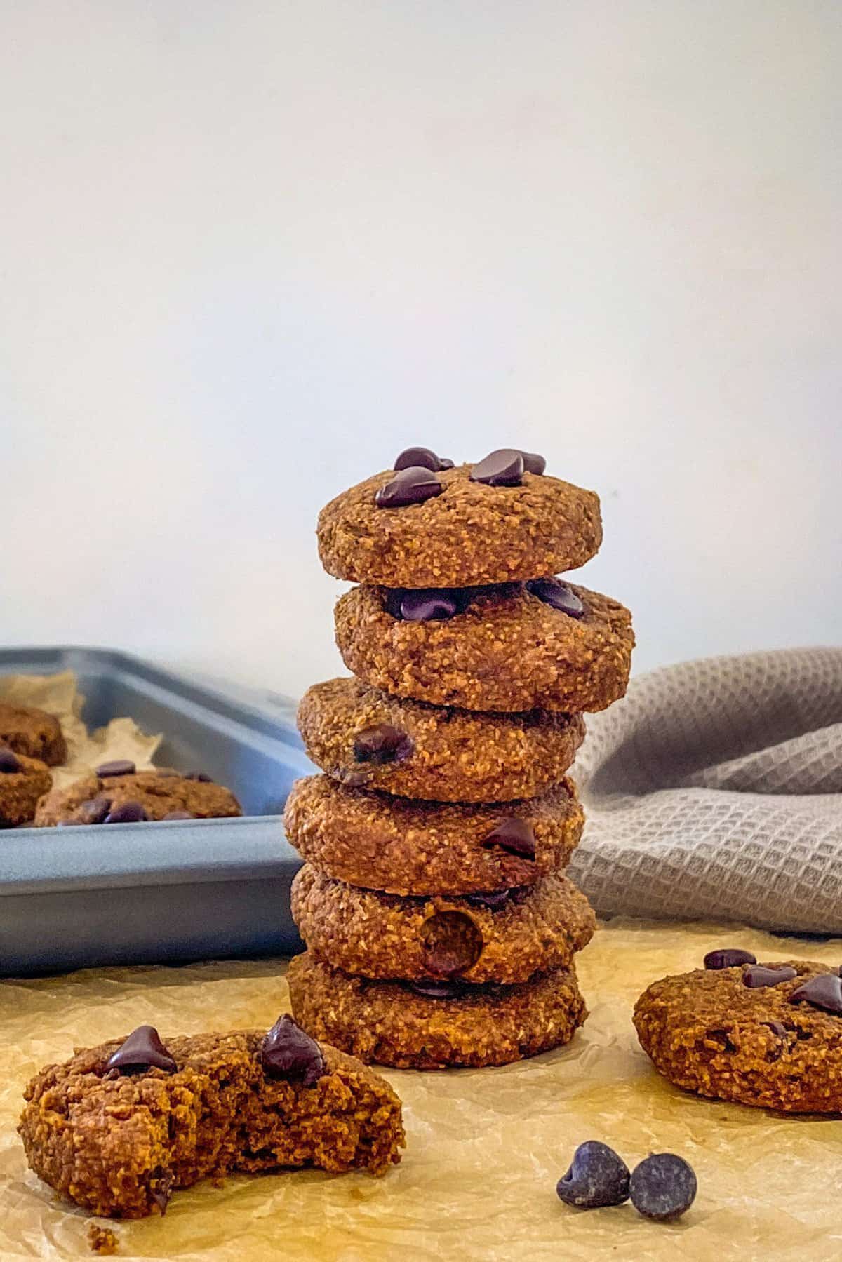 Stack of chocolate chip cookies with tray of more cookies in background.