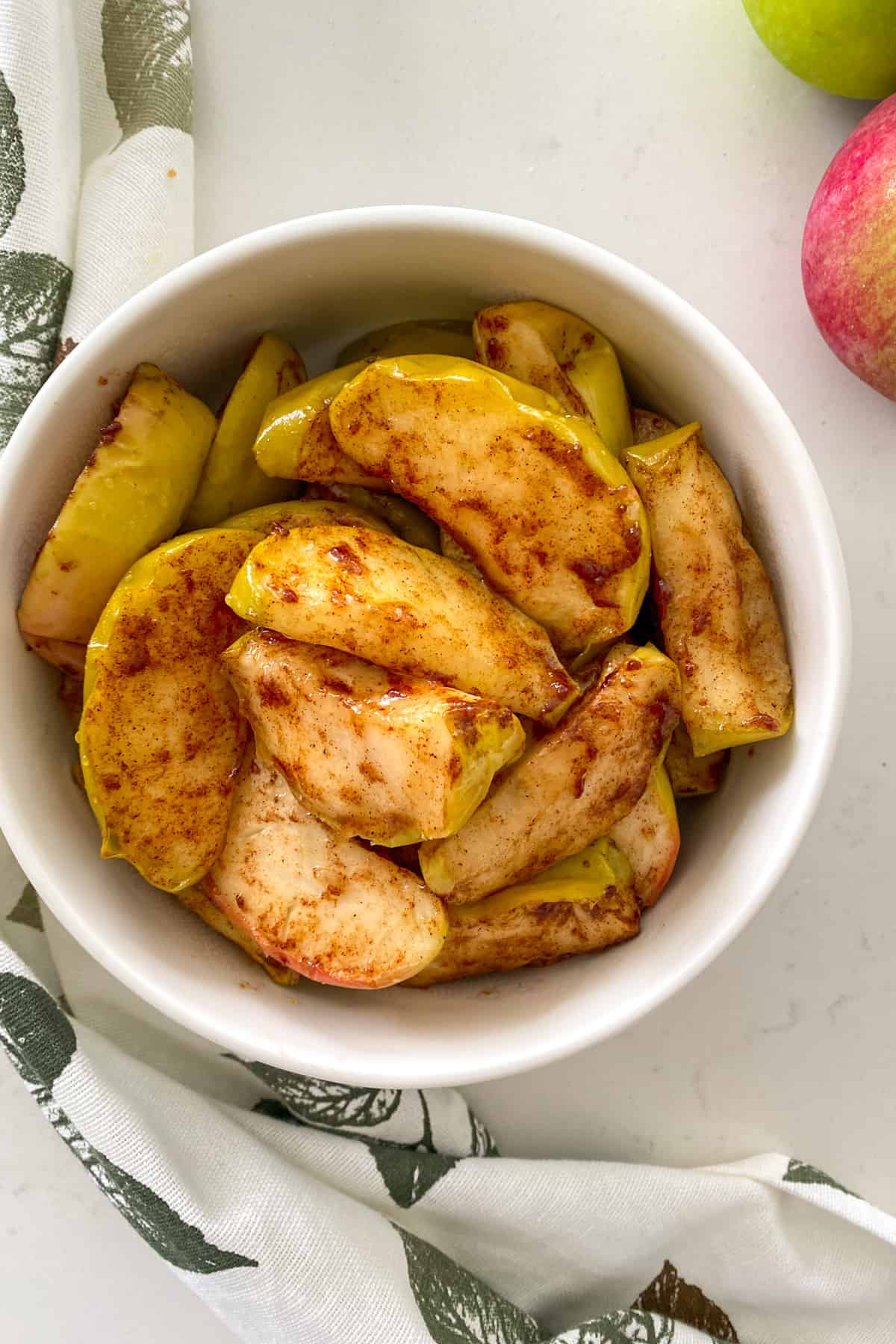 Apple wedges coated in sweet marinade in white serving bowl.