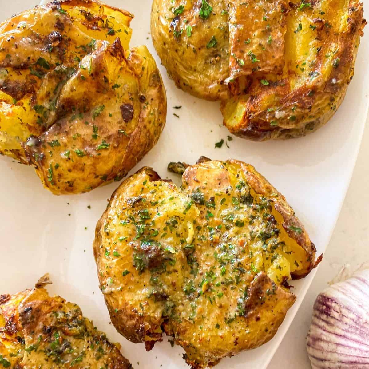 Smashed potatoes on white serving dish with parsley sprinkled on top.