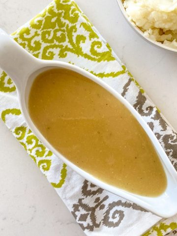 Gravy boat filled with golden colour gravy resting on dish towel.