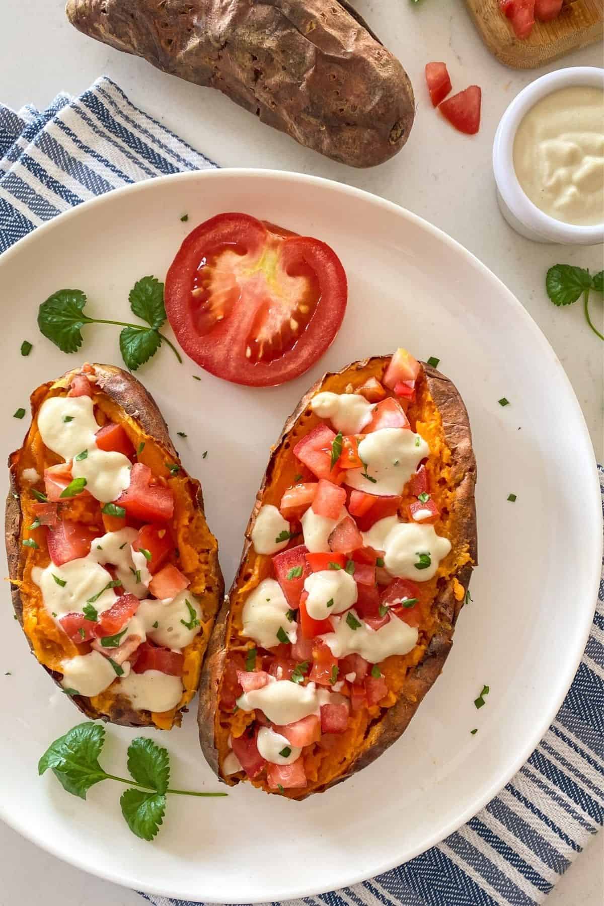 Baked sweet potatoes in white plate with sour cream, tomato and parsley on top.