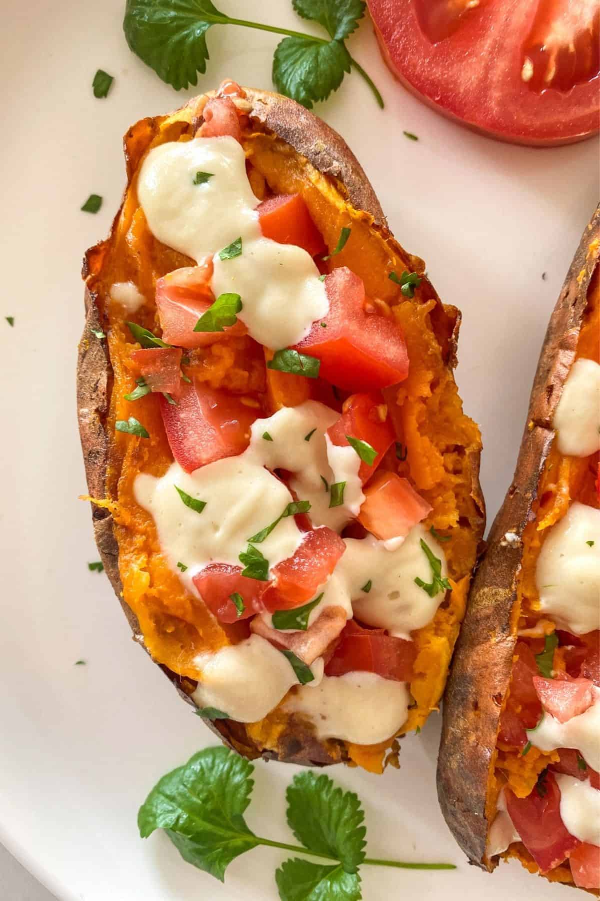 Close up of whole baked sweet potato sliced open and loaded with tomato, sour cream and parsley garnish.