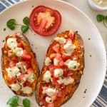 Baked sweet potatoes in white plate with sour cream, tomato and parsley on top.