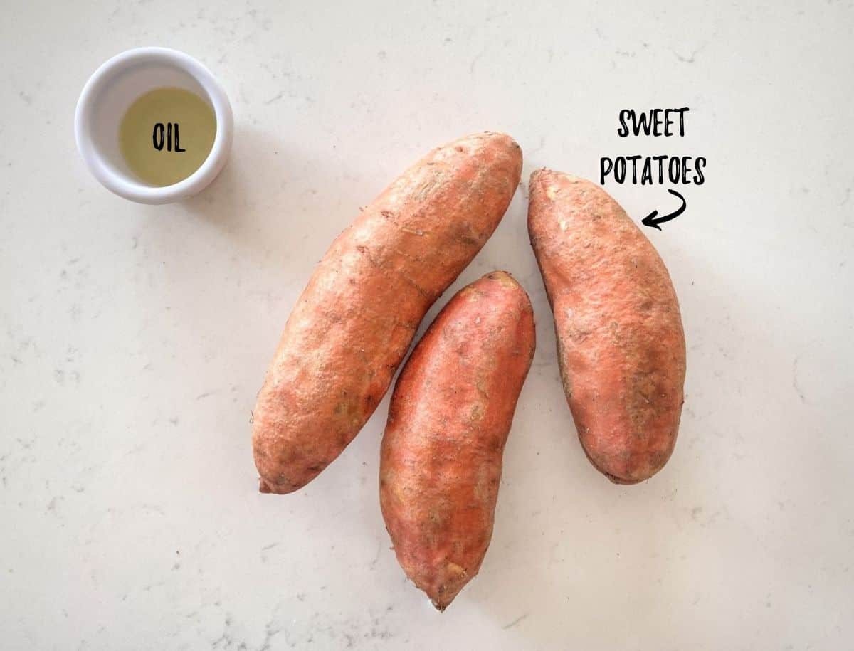 Three sweet potatoes on countertop and small bowl with oil inside.