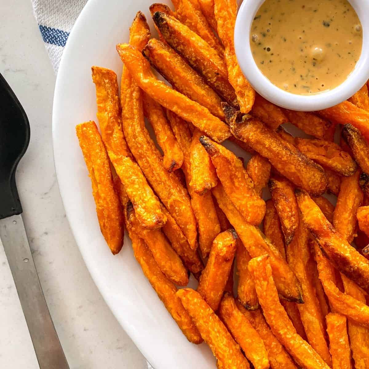 Sweet potato fries in serving dish with orange coloured dip beside them.